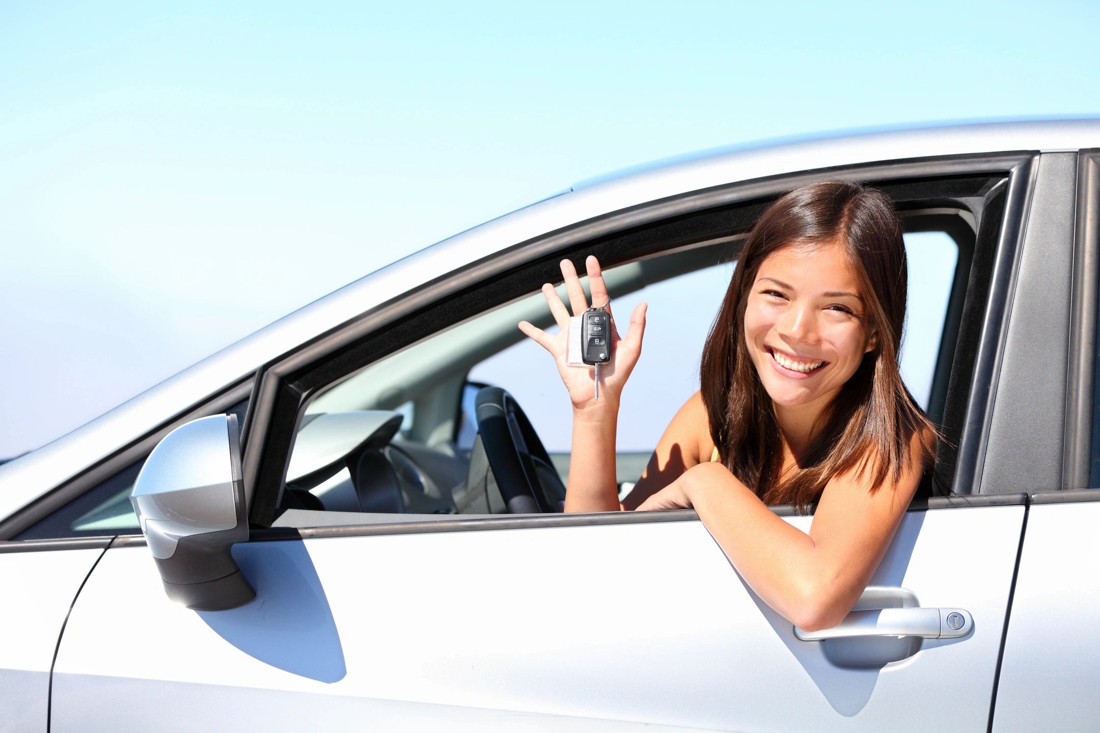 A woman sitting in her car holding up the keys.