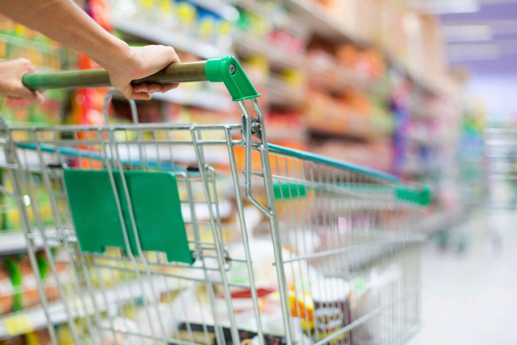 A person pushing a shopping cart in the aisle of a grocery store.